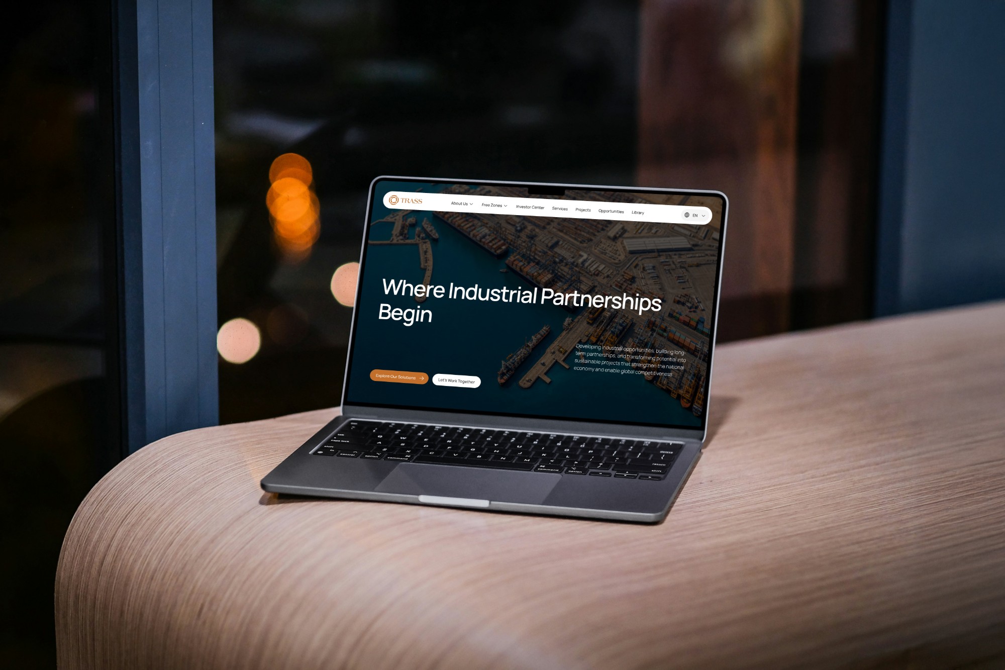 A laptop on a wooden table showing the Trass homepage
